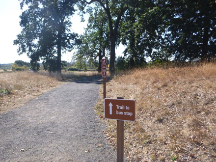 Sign says “Trail to bus stop” - compacted gravel trail from main parking lot